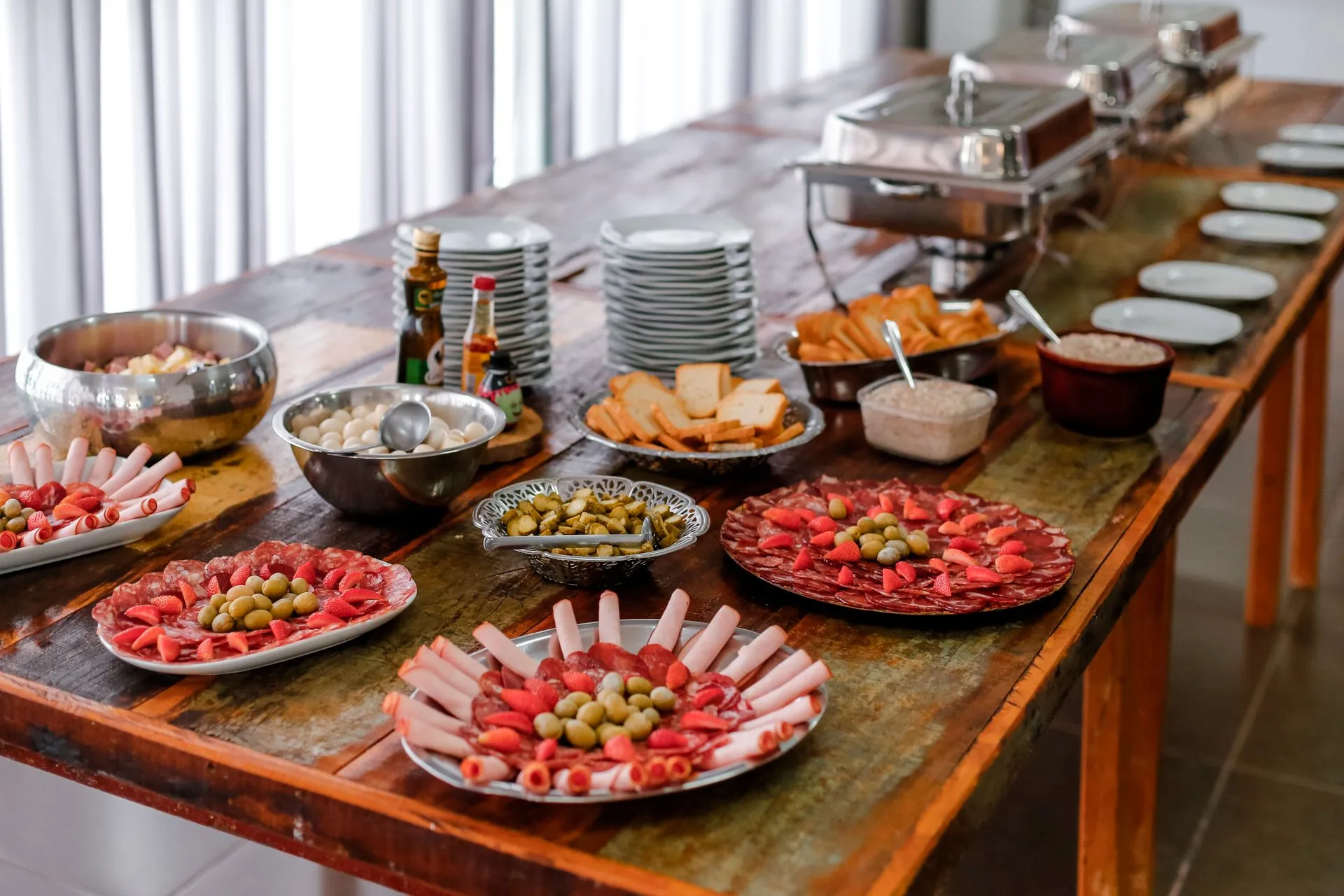 Cold cured meat platters, olives, and appetizers on a rustic wooden buffet table for event catering
