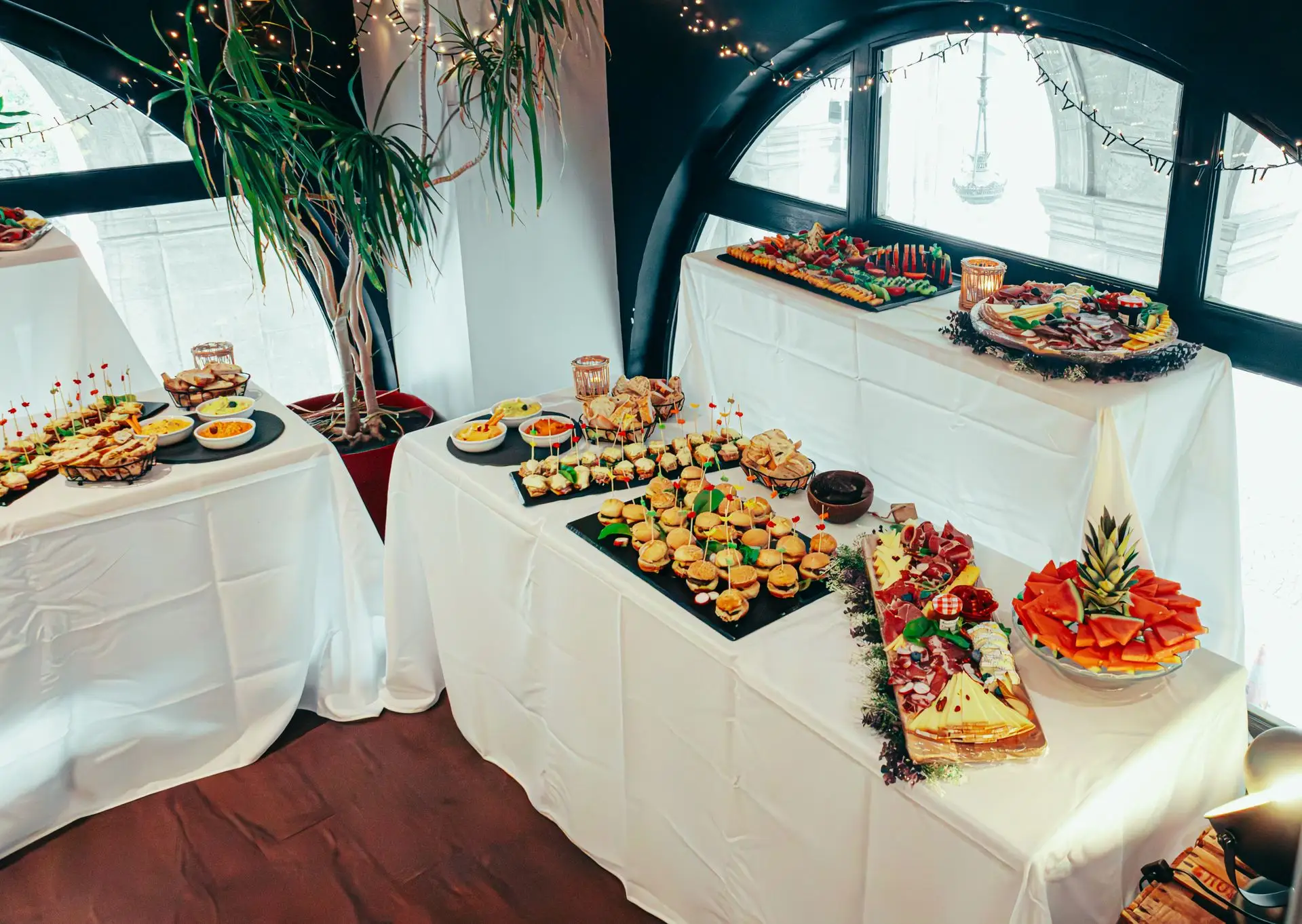 Assorted finger food canapés, mini burgers, and fruit platters displayed on white linen catering tables